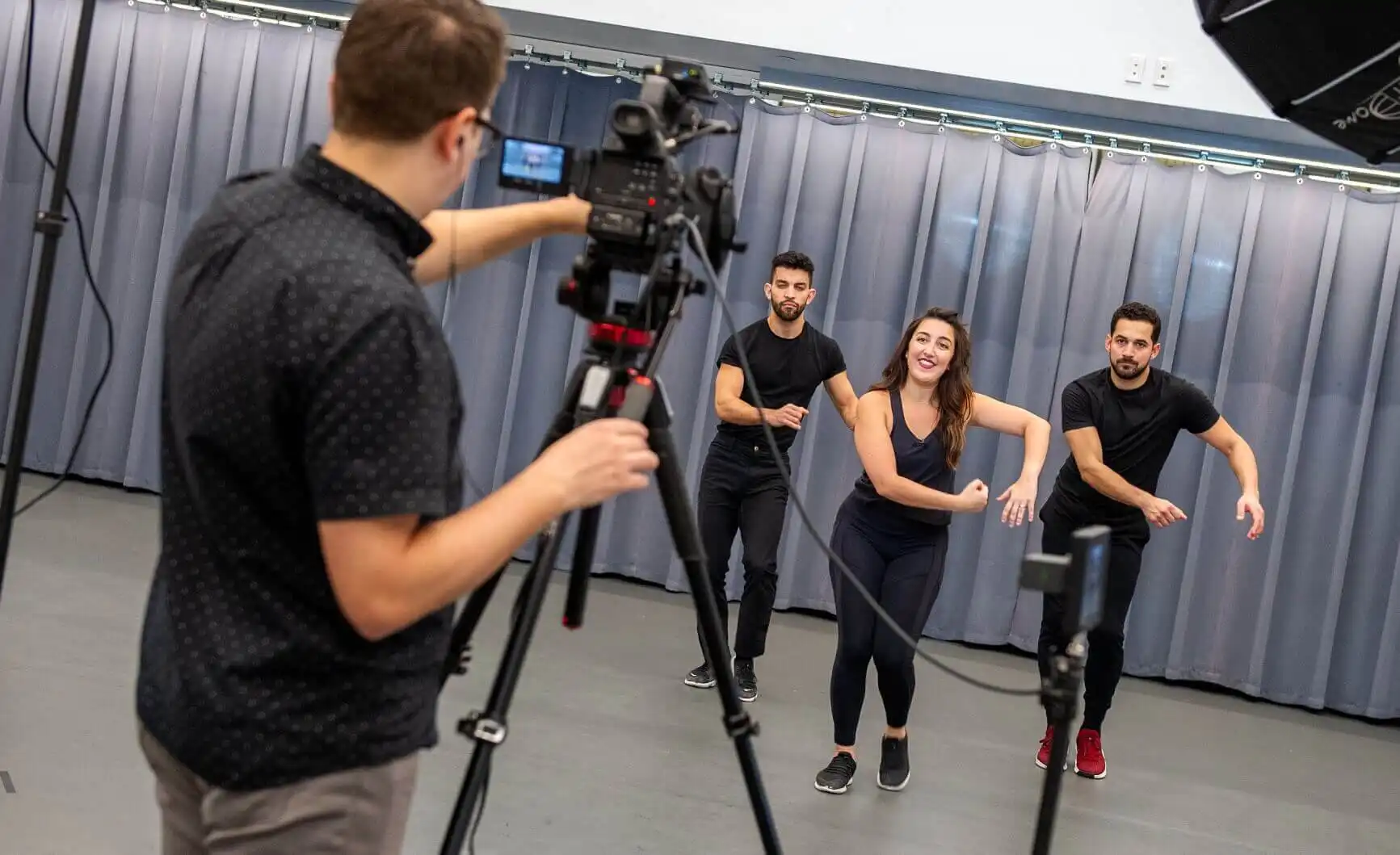 A man filming three people dancing with a video camera on a tripod.